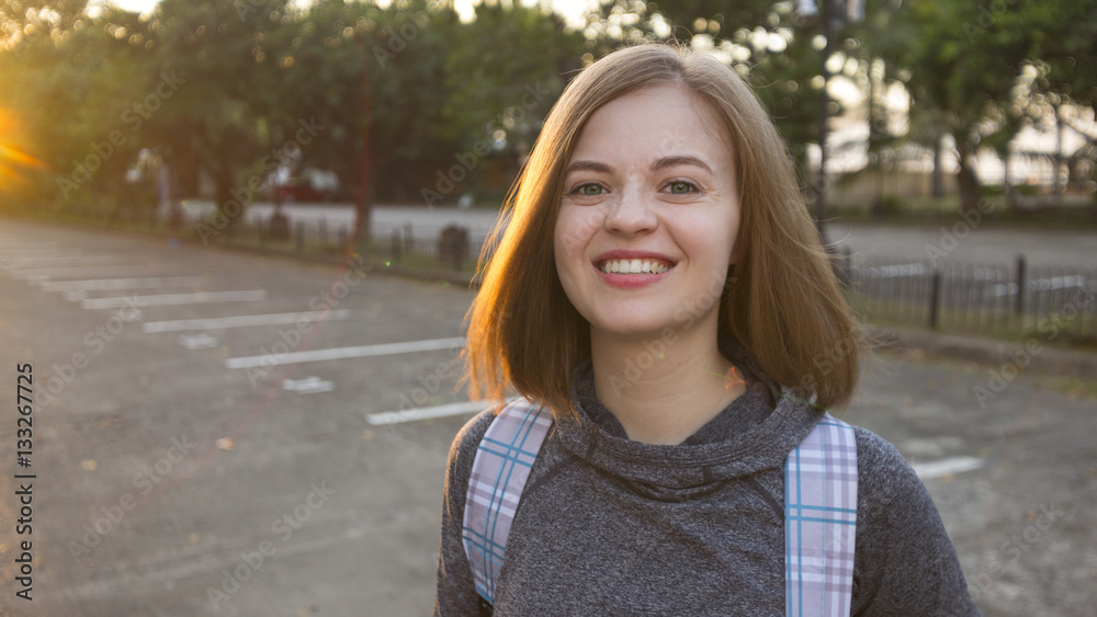 Portrait of smiling beautiful girl with bob hairstyle and green eyes in sport jacket and backpack standing near Harbour Square, popular tourist place in Manila, Philippines. Green trees on background Portrait of smiling beautiful girl with bob hairstyle and green eyes in sport jacket and backpack standing near Harbour Square, popular tourist place in Manila, Philippines. Green trees on background