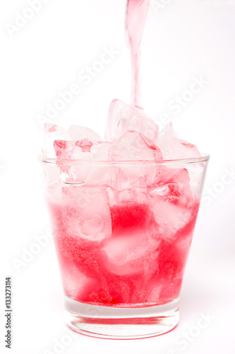 Pouring red sparkling wine in a glass with dancing bubbles on ice cubes isolated on white background
