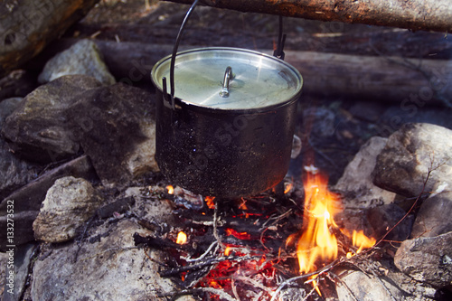 Cauldron boils on the fire in the forest. In marching a saucepan preparing food. Adventure tourism, camping, cooking on a fire. Survival in the forest. Stalker