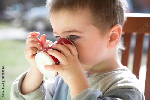 Baby boy drinks  red-white mug  outdoor  natural light