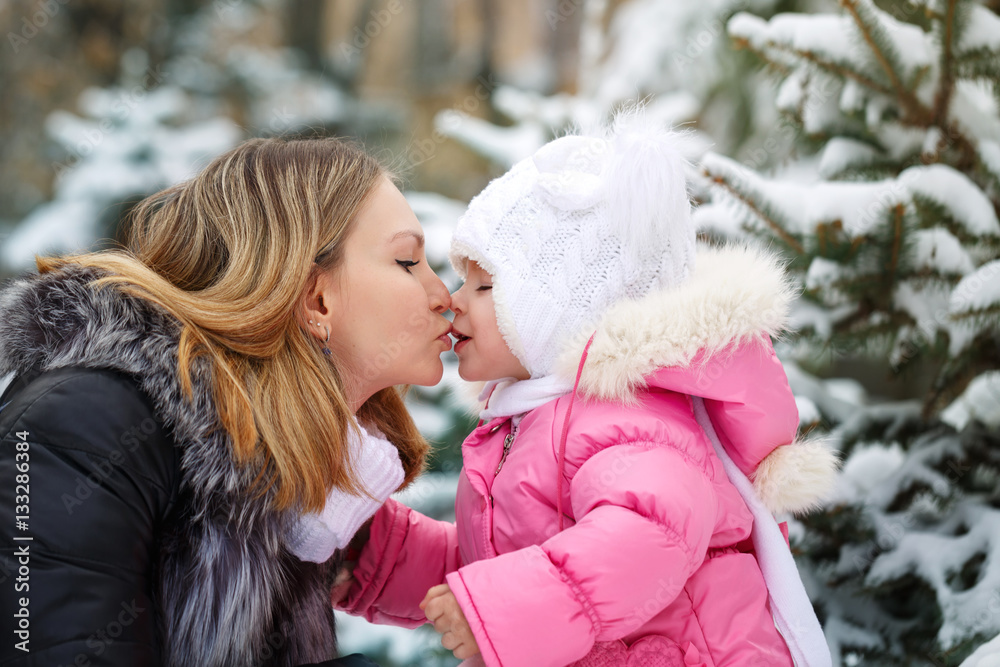 Mother kissing daughter in the nose outdoors. Family walk in a winter park. Family happiness.