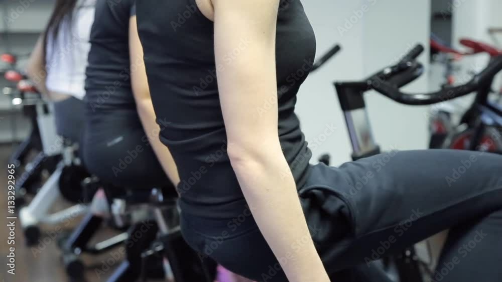 Three athletes actively pedaling on a stationary bike at the gym. Three athletes actively pedaling on a stationary bike at the gym.