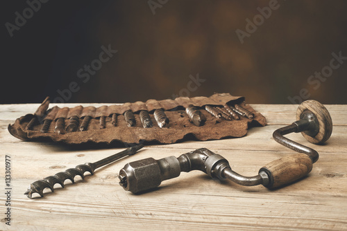 Drill brace with bits in leather tool roll on a wooden workbench