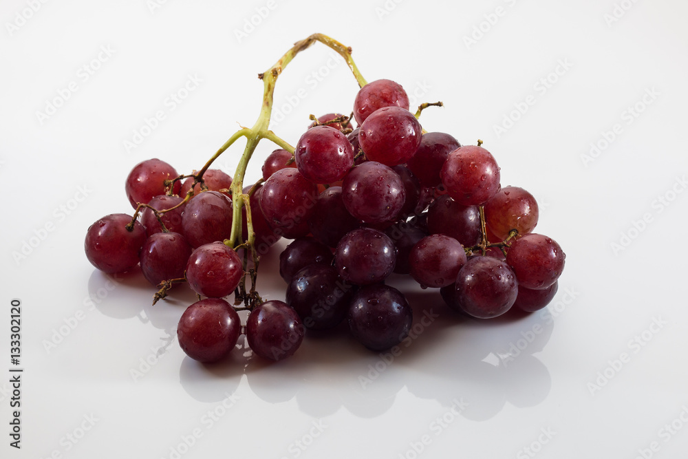 Isolated red grapes against a white background casting a reflection