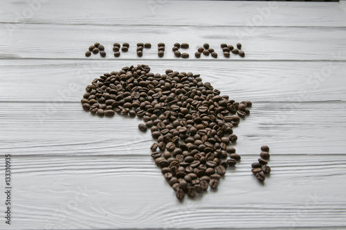 Map of the Africa made of roasted coffee beans laying on white wooden textured background and space for text