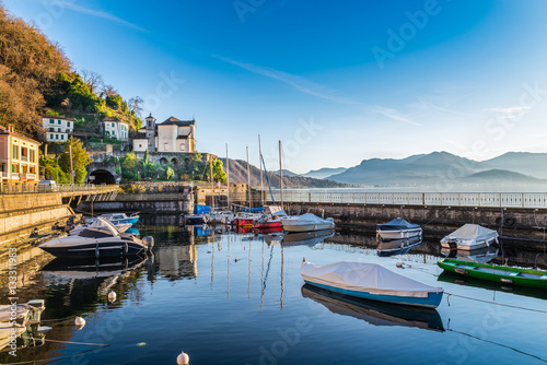Maccagno on lake Maggiore (Verbano) with the old small harbor and the Sanctuary Madonna della Punta, province of varese, Italy. On the background the village of Luino