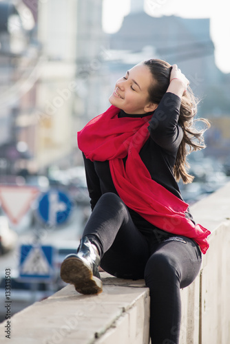 Young girl dressed in casual chinos, black sneakers and walking on a street with wall in background.