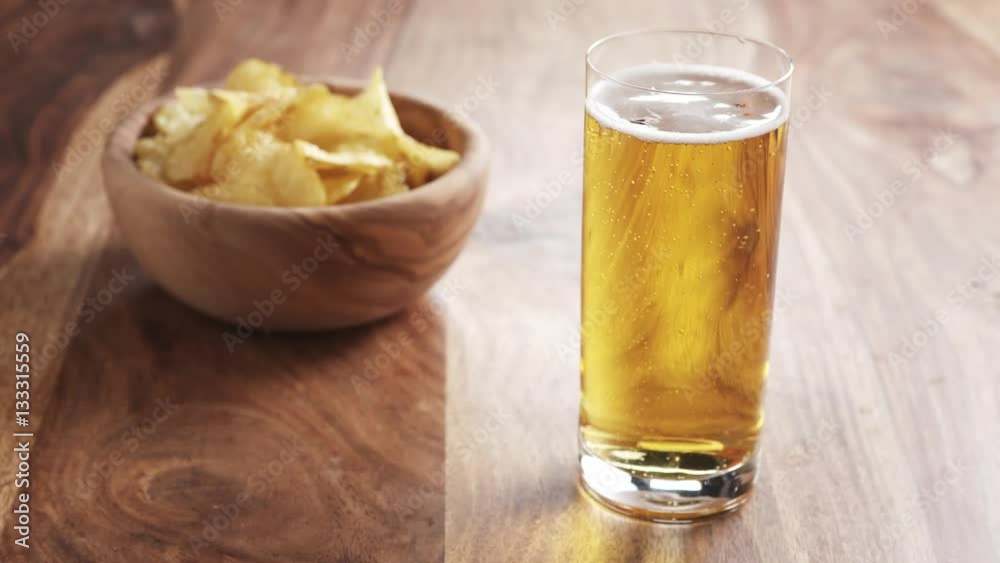 lager beer poured in glass on wooden table with potato chips in slow motion, 180fps prores footage