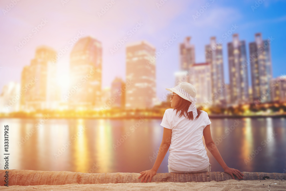 Obraz premium Woman sitting in the city park near the river looks at the town