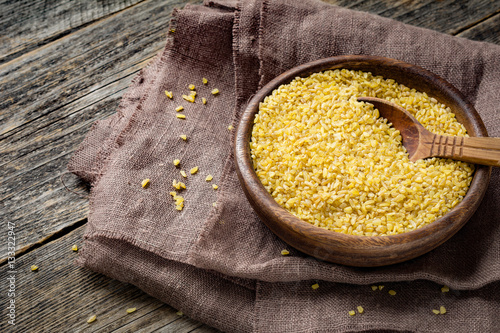 Uncooked bulgur in wooden bowl on wooden table background, rustic style. Bulgur wheat grains