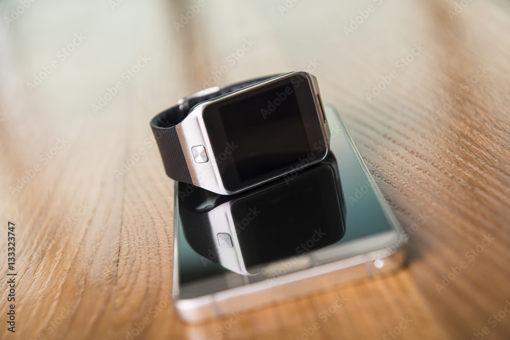 Smartwatch placed on a smartphone on the wooden table. Smartwatch placed on a smartphone on the wooden table.