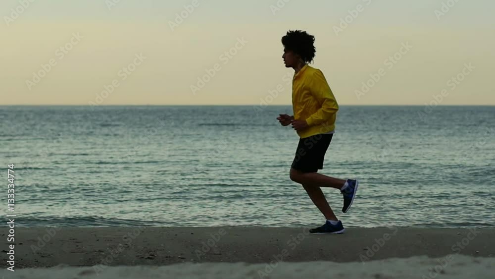 young African-American man is running along the beach at dawn
