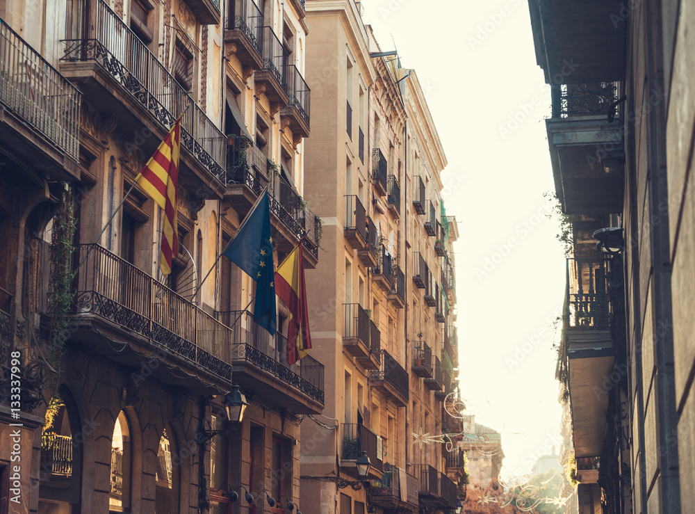 alley at barcelona with some spain and europe flags on building in warm sunlight