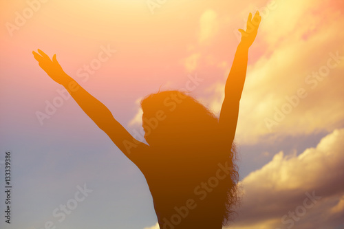 Silhouette of a beautiful girl who is holding out his hands to the sides against the bright, cloudy sunset