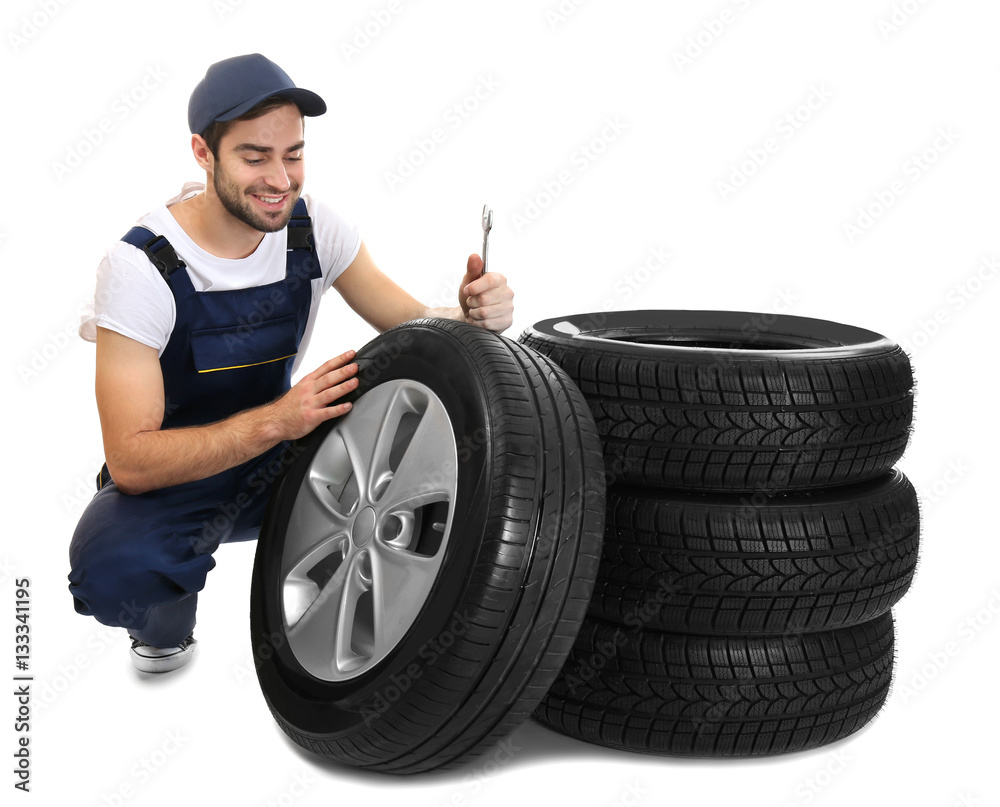 Young mechanic in uniform with wheels on white background