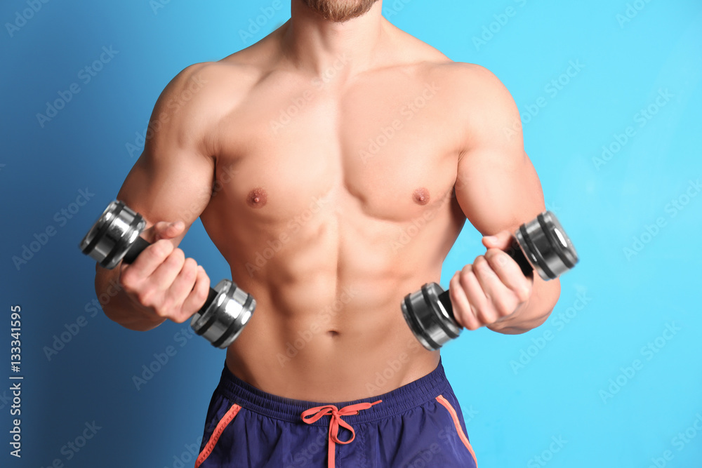 Sporty young man with dumbbells on color background, closeup