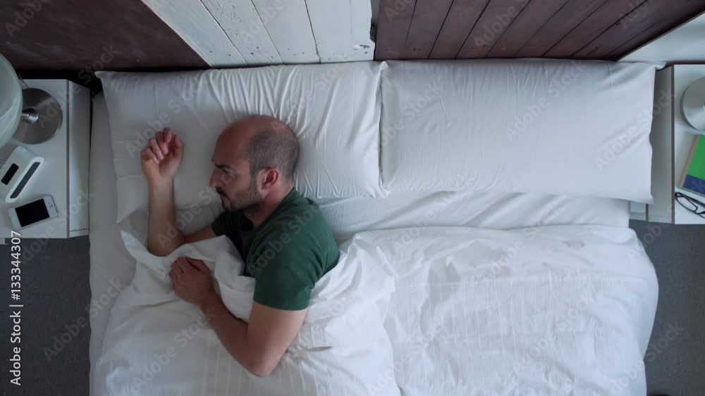 Young man is sleeping in the morning when ring the alarm. She switches off it and gets up happy.