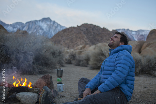 An adult man stretching and keeping warm by his campfire in the Alabama Hills. Lone Pine, California.