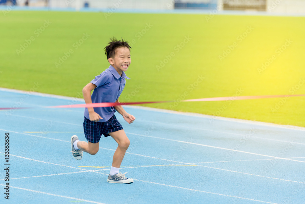 Obraz premium Young Asian boy running on blue track in the stadium