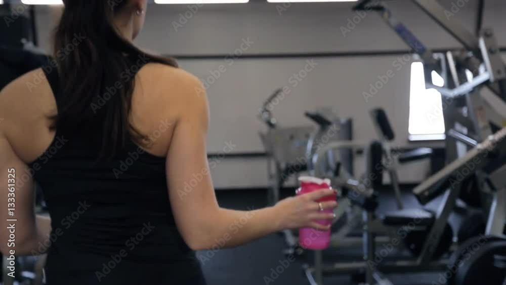 Shooting from back woman walking drinking water in gym Shooting from back woman walking drinking water in gym