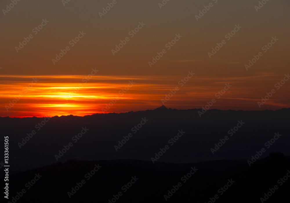 Fiery sunset from mountain pick with thin glazes in the sky evening. Fall season. Orobie alps. Rena pick. Bergamo Italy. In the distance the Monviso.