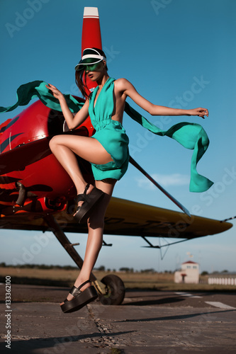 fashion pilot girl in a visor next to propeller plane during sunset
