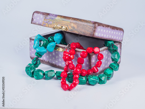 Picture of the opened purple-coloured box for bijouterie with turquoise, malachite and coral bead necklaces on white background. Handmade decoupage jewel box. Side view. photo