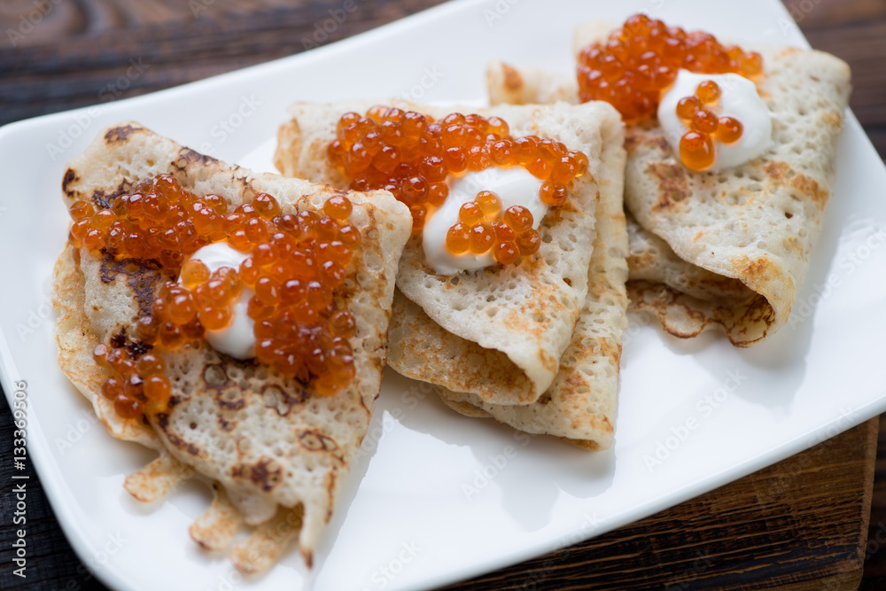 Close-up of crepes topped with sour cream and red caviar