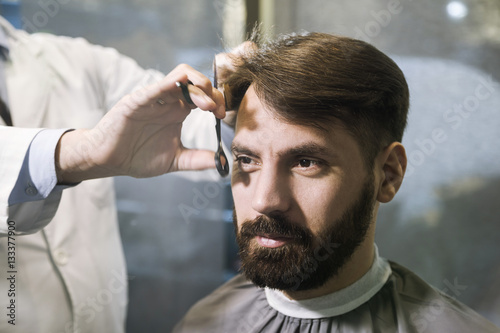 Front view of a bearded businessman having his hair cut in a barber shop. Concept of being well groomed