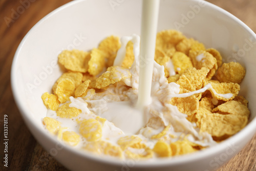 milk pour into bowl with corn flakes, preparing breakfast