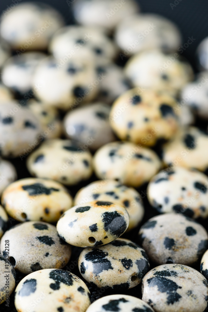 Collection of spotted Dalmatian jasper coin beads on black weave.