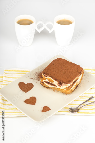 Tiramisu    Tiramisu cake in a plate with a cocoa decoration and two cups of coffee on a white background