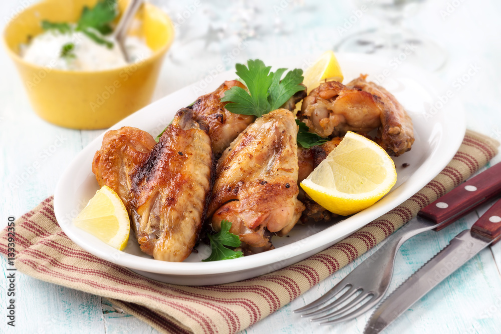 Grilled chicken wings with lemon slices and parsley on a white oval plate Grilled chicken wings with lemon slices and parsley on a white oval plate
