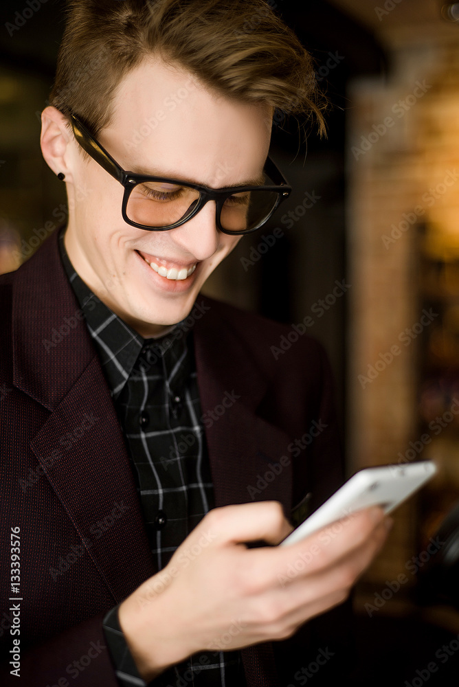 attractive young hipster in glasses looking at a smartphone and smiles