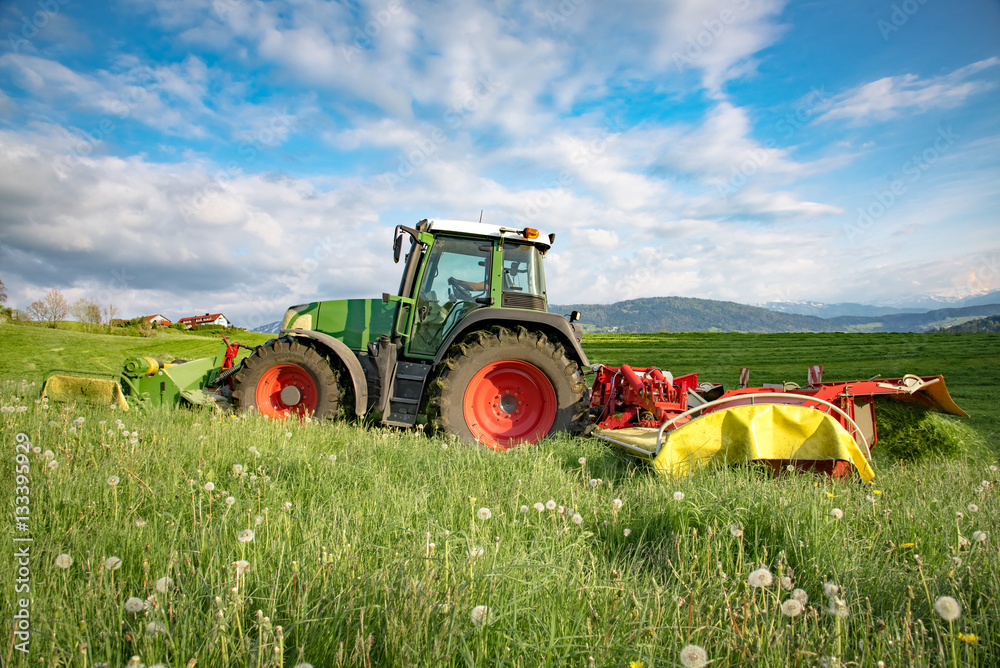 Heuernte - Traktor mäht Gras auf einer Wiese im Allgäu Heuernte - Traktor mäht Gras auf einer Wiese im Allgäu