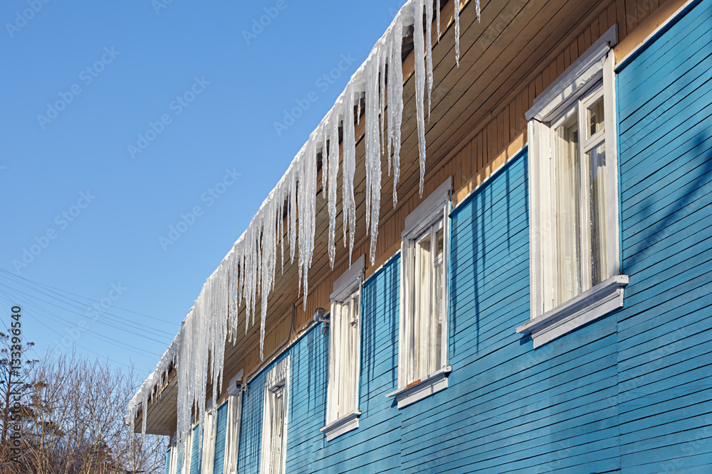 Dangerous icicles hanging from the roof of a wooden house