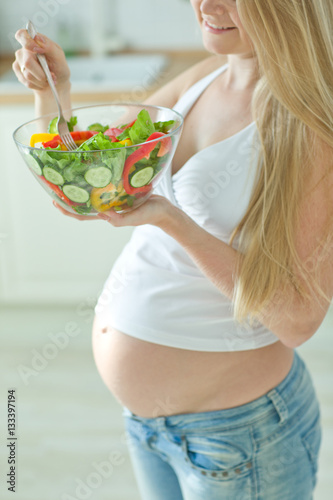 Pregnant woman holding glass bowl with fresh salad 