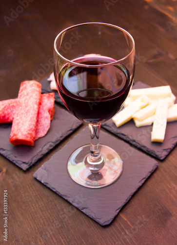 Slices of salami and wine on slate plates on a wooden table seen up close
