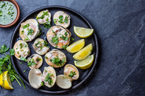 Raw clams with lemon, herbs and white wine, slate background
