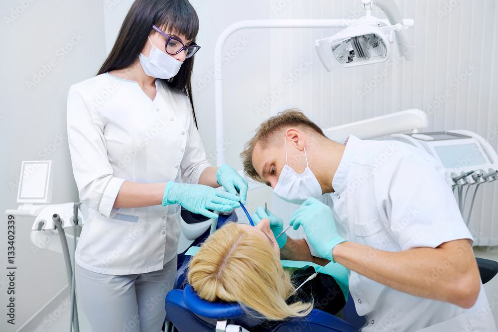 Dentist man with assistant treats teeth patient in hospital office Dentist man with assistant treats teeth patient in hospital office