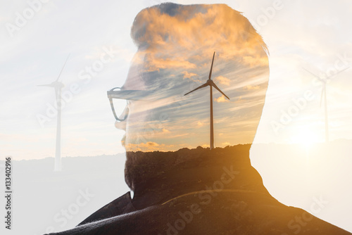 Double exposure portrait of a businessman thinking about renewable electricity combinated with sunset landscape and winmills