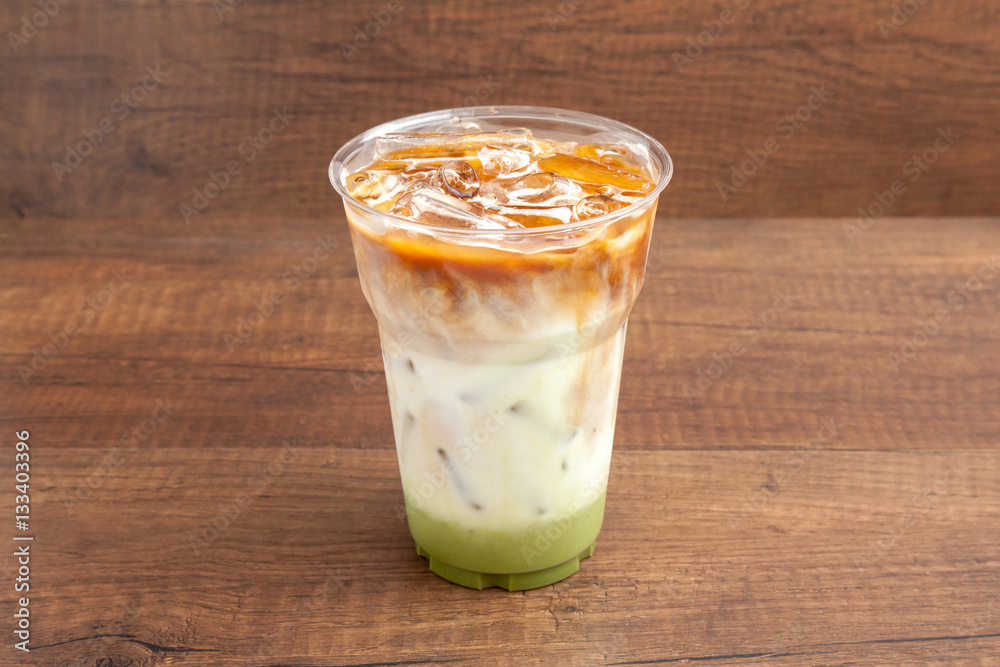 Iced matcha and espresso latte in plastic glass on wooden background Iced matcha and espresso latte in plastic glass on wooden background