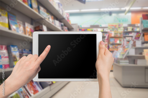 human hand hold and touch blank screen smart phone, tablet, cell phone on blurry bookstore.