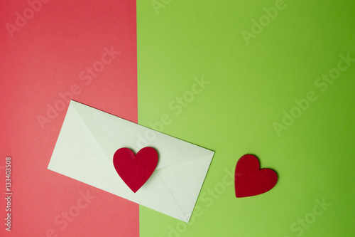 Envelop with two hearts on greenery and red colored paper background. Top view. Copy space for text