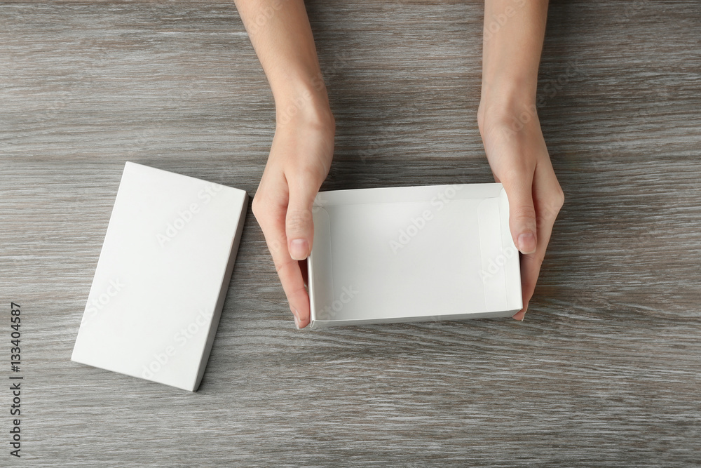 Female hands with white open box on wooden background Female hands with white open box on wooden background