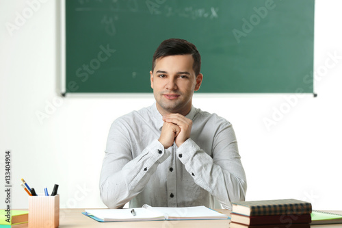 Handsome young teacher sitt...