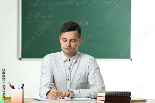 Handsome young teacher sitt...