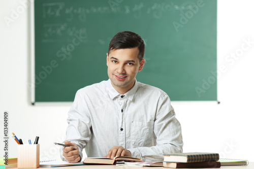 Handsome young teacher sitt...