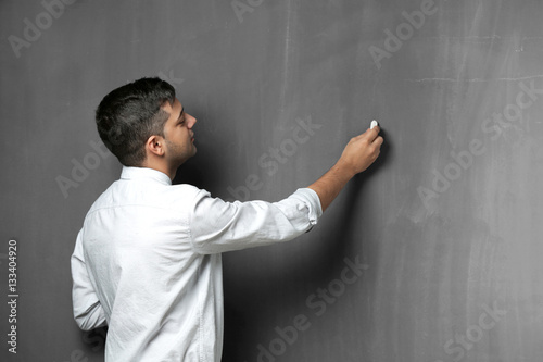 Handsome young teacher writing on blackboard