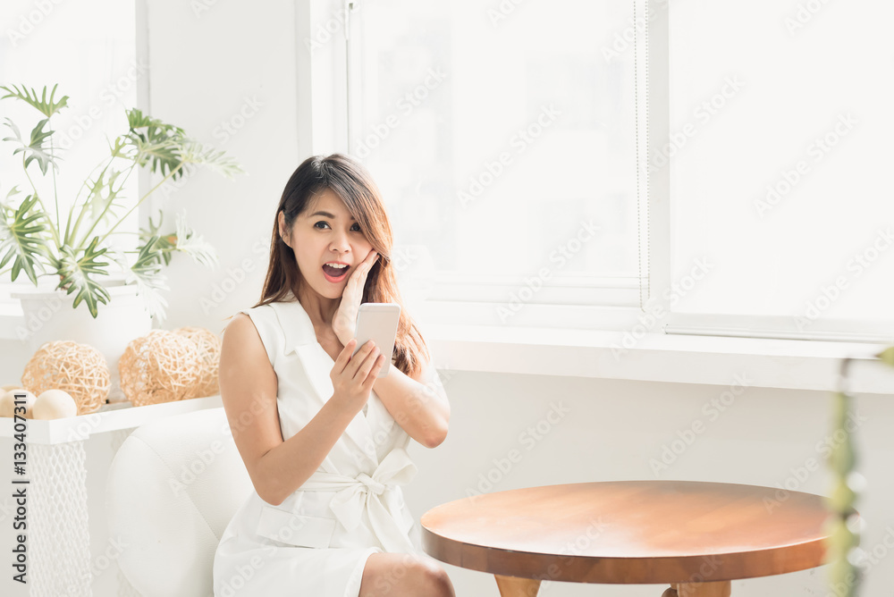 Asian woman surprised and shocked while using smart phone in white room Asian woman surprised and shocked while using smart phone in white room